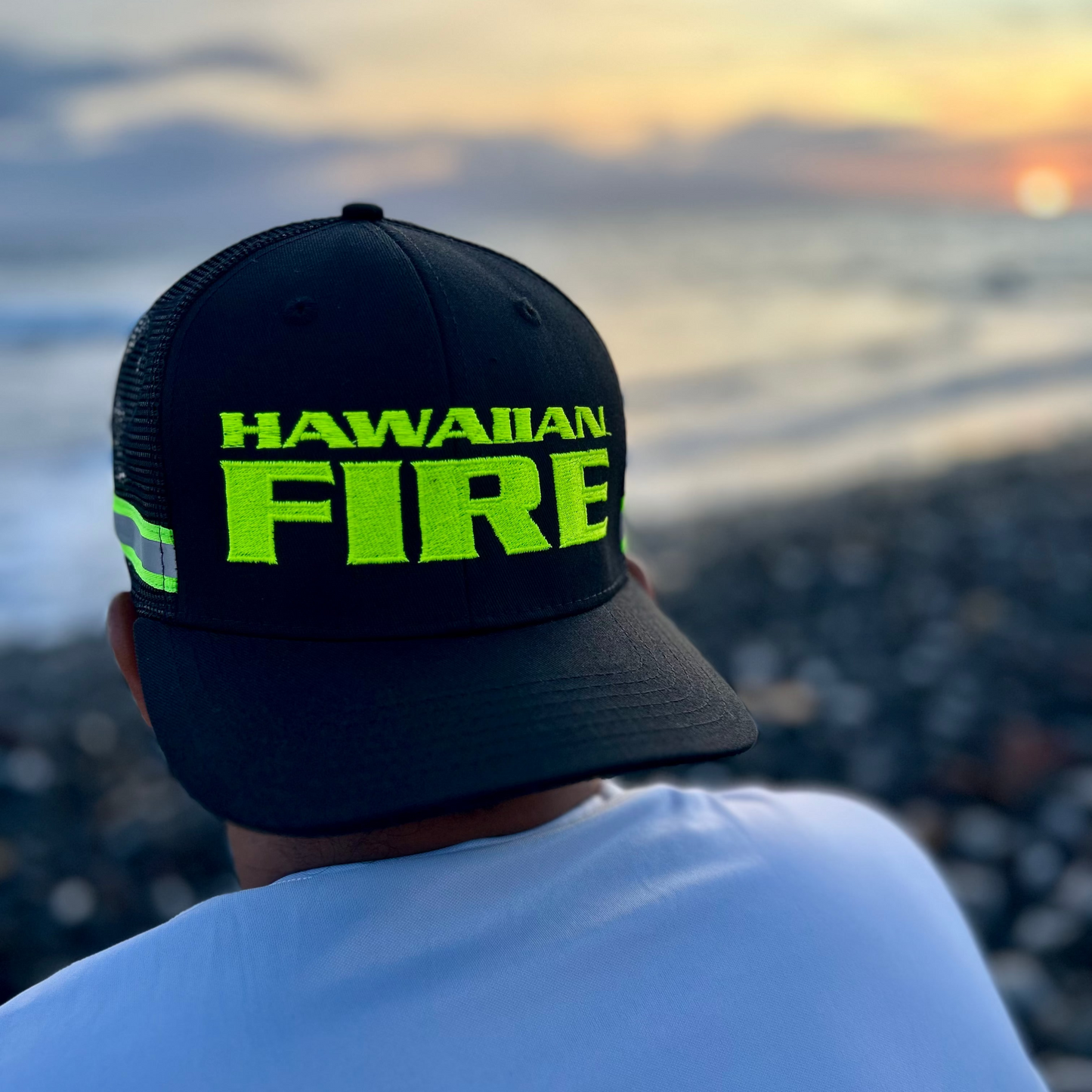 Person wearing a black cap with 'Hawaiian Fire' text, overlooking a scenic view.